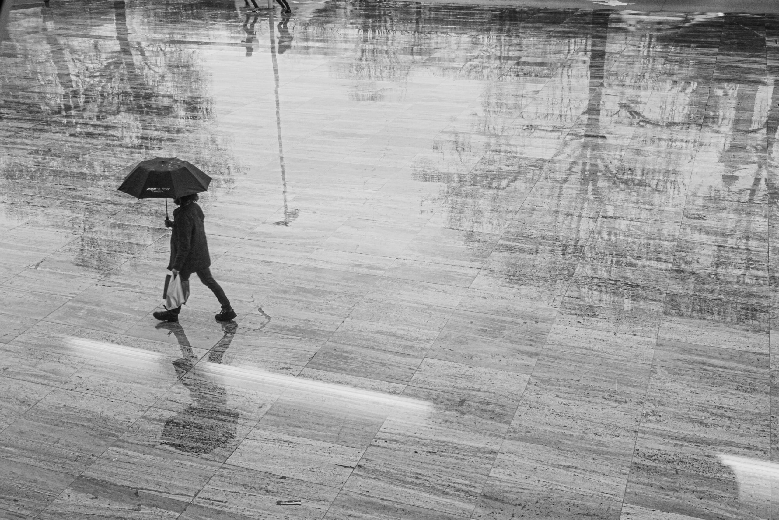 Rainy day in Porto, Portugal, with a pedestrian carrying an umbrella across a wet public square.