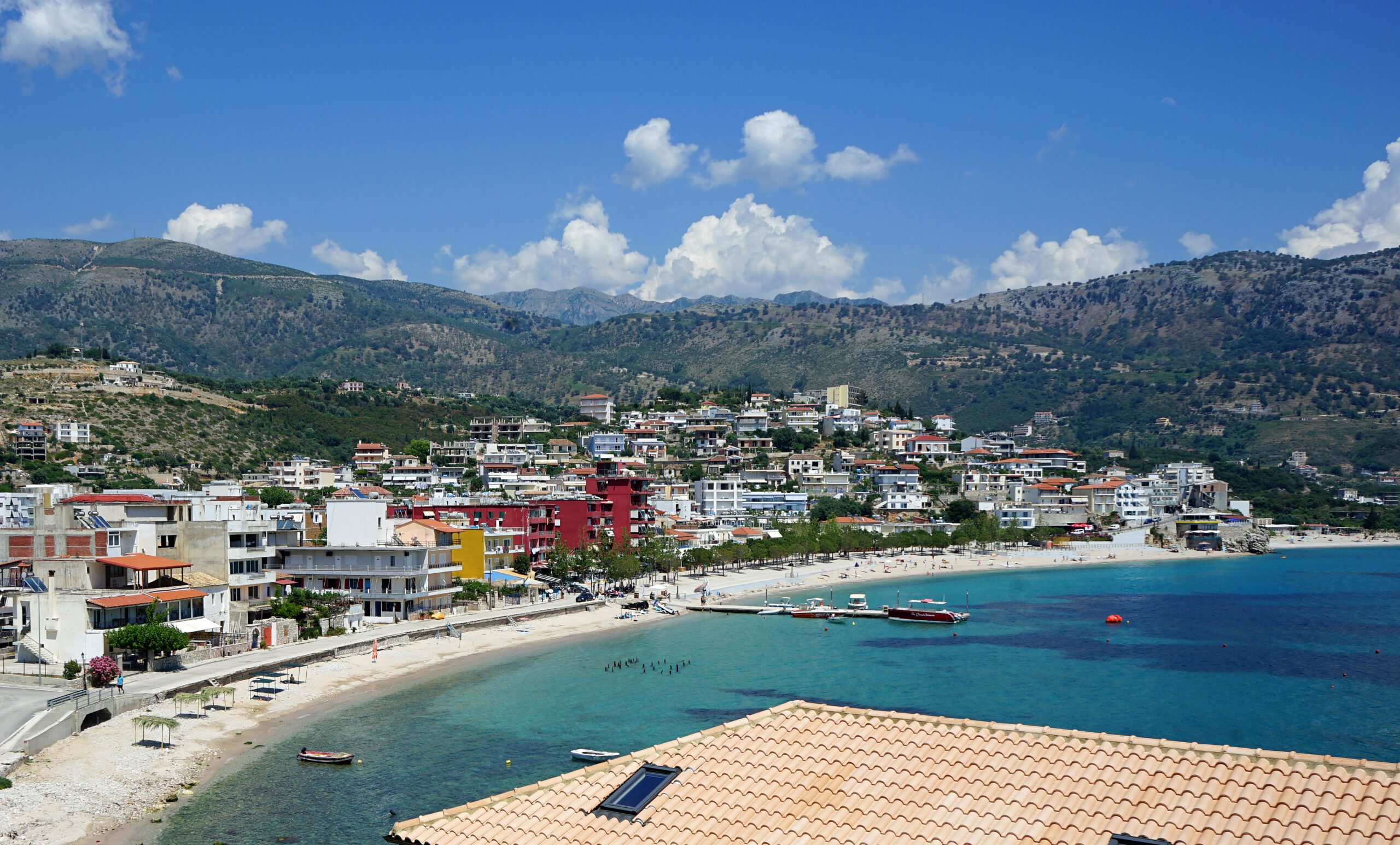Bright coastal panorama of Himarë with turquoise water, beach, and hillside homes.
