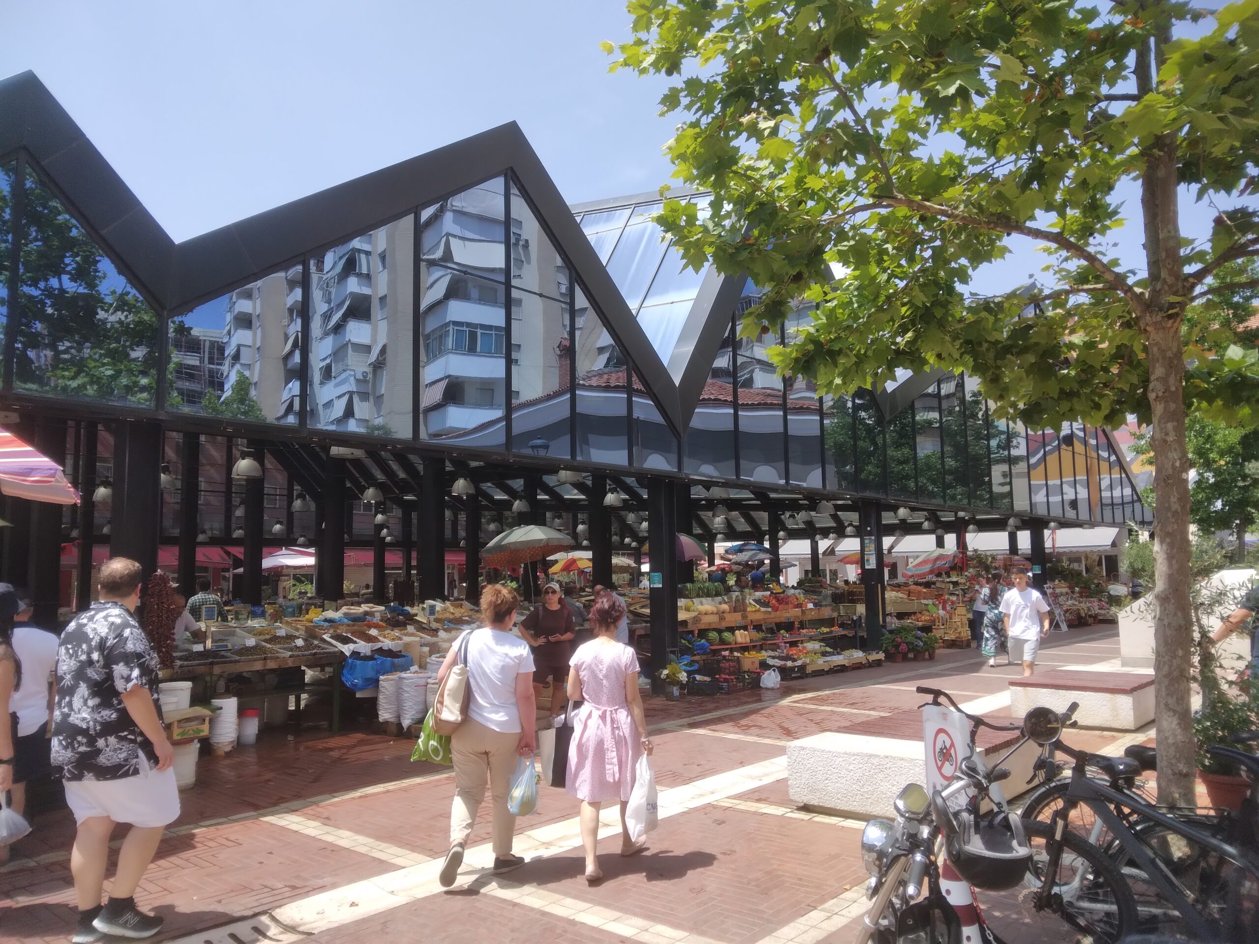 Covered produce stalls and shoppers at New Bazaar in Tirana on a bright day.