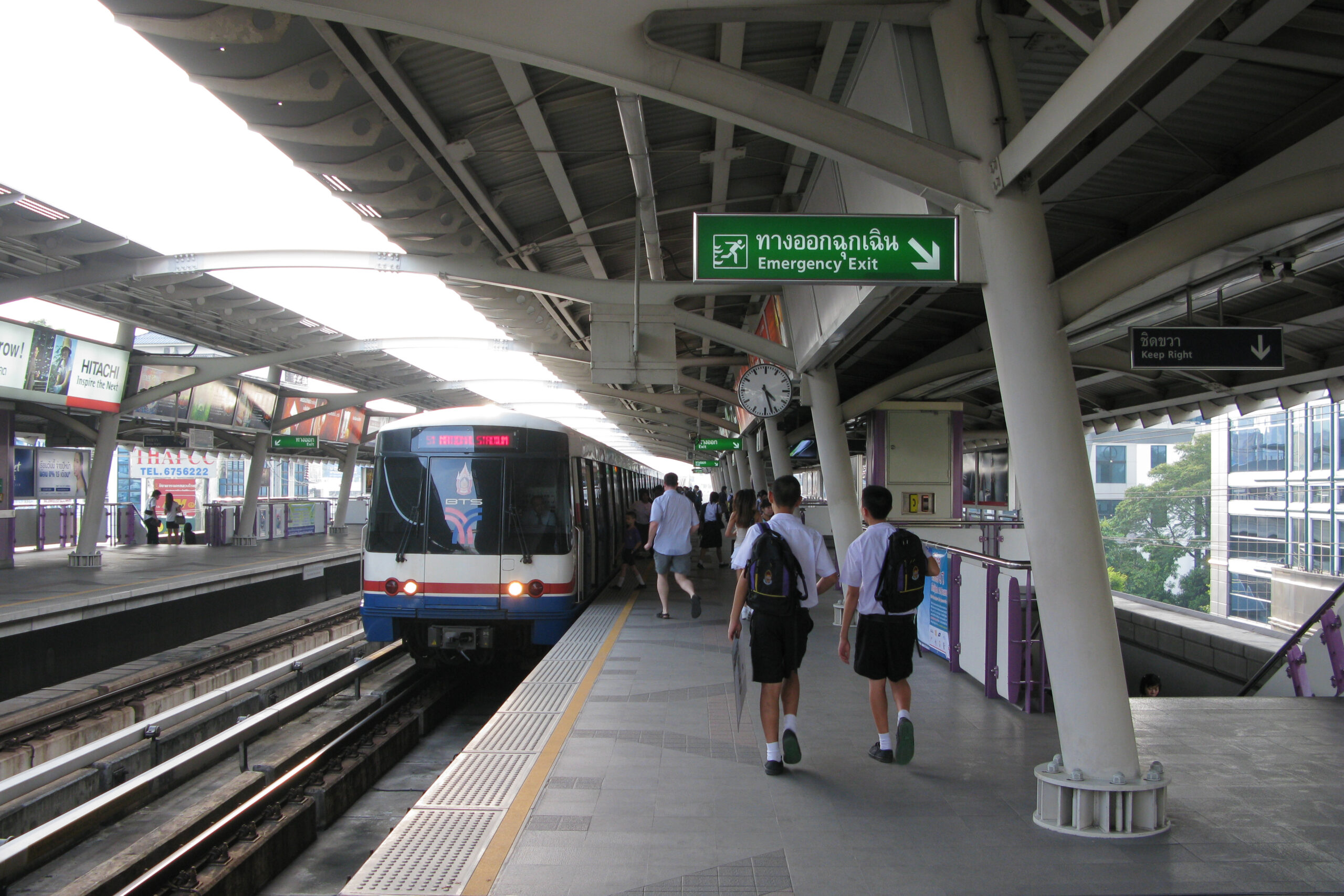 Bangkok BTS Skytrain station platform with tracks, signage, and an elevated city view.