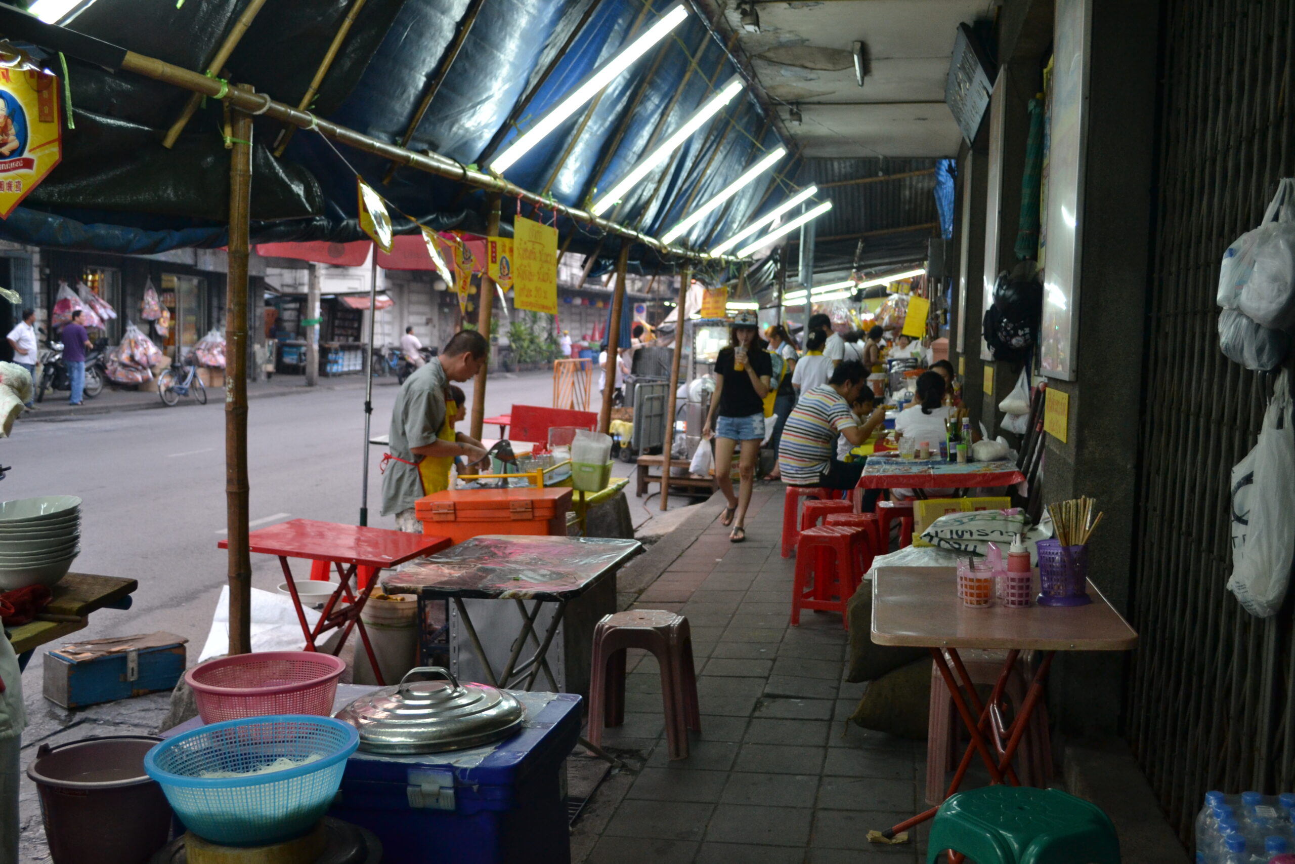 Everyday Bangkok street scene with food stalls, tables, and neighborhood activity after dark.