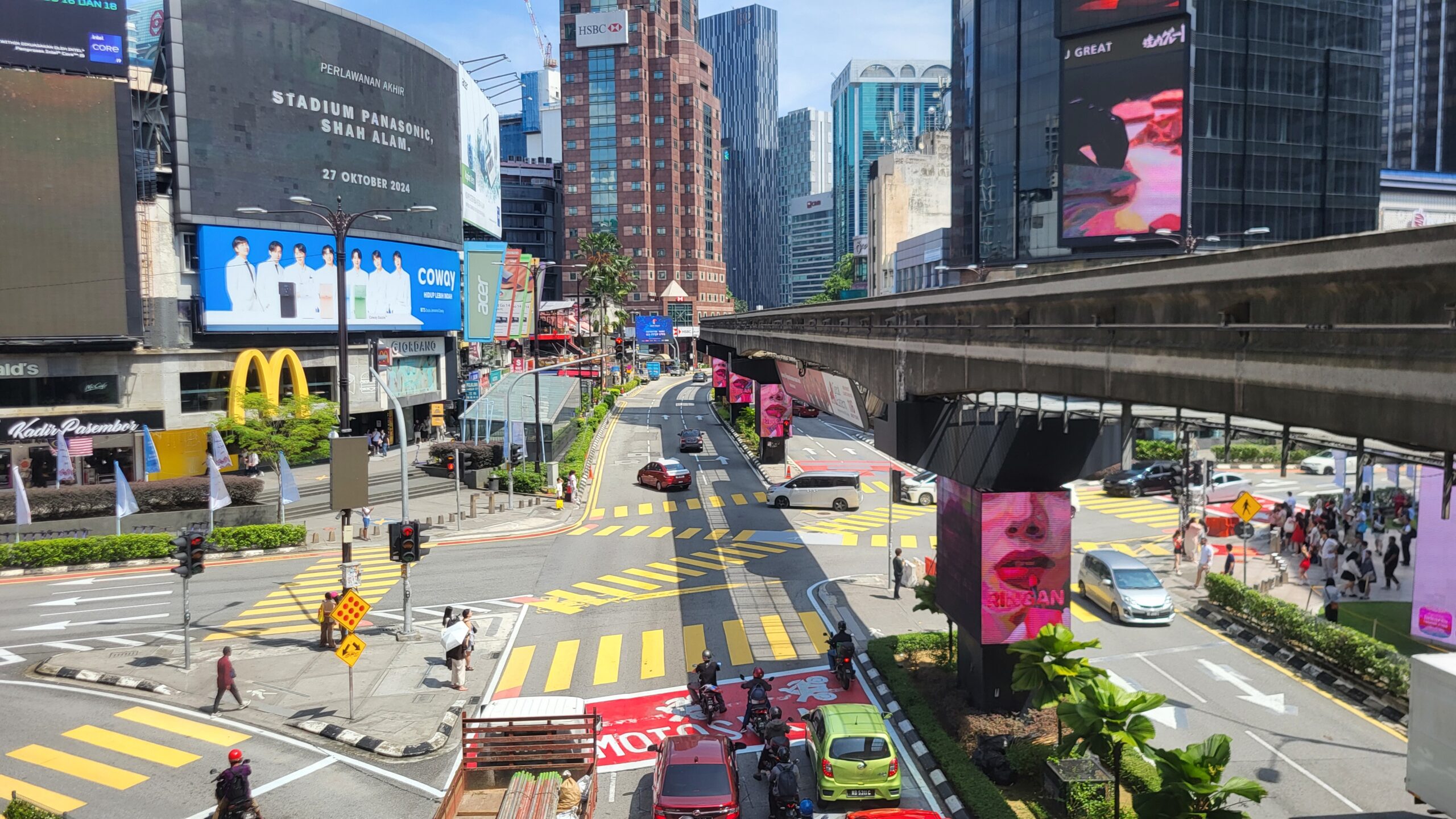 Busy Bukit Bintang junction in Kuala Lumpur with shops, signs, greenery, and everyday pedestrian movement.