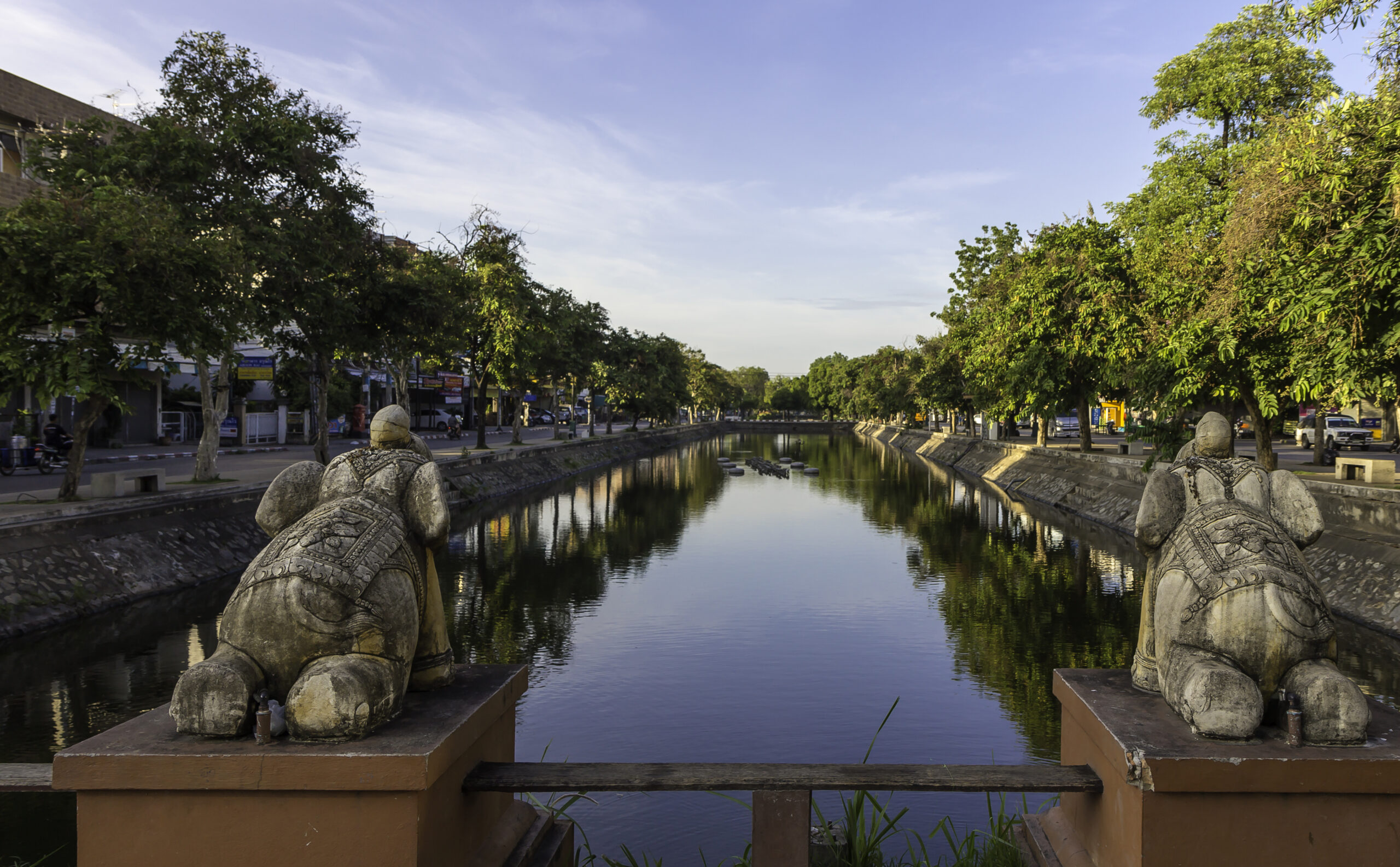 Tree-lined stretch of Chiang Mai moat with water and greenery in daylight.