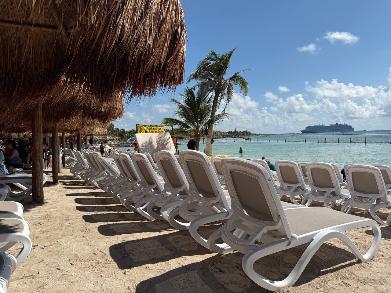 Beachfront view in Costa Maya with loungers, palms, and a cruise ship visible offshore.