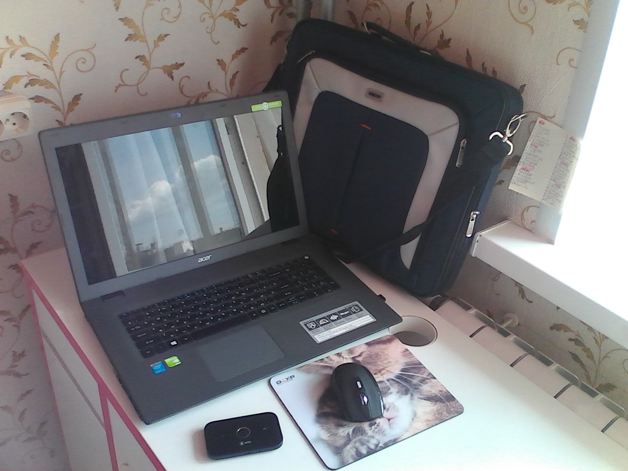 Laptop, bag, and router arranged on a desk for checking internet reliability.