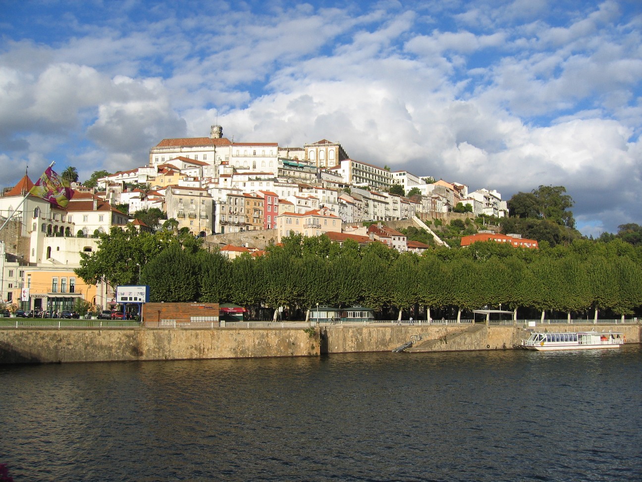 Wide view of Coimbra rising above the river under a bright sky.