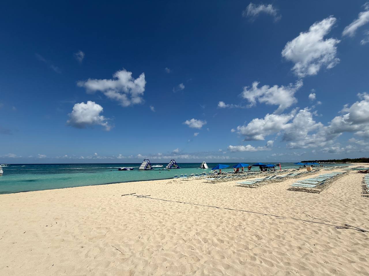 Wider beach view in Cozumel with open sand, umbrellas, and bright Caribbean water during a catamaran stop.