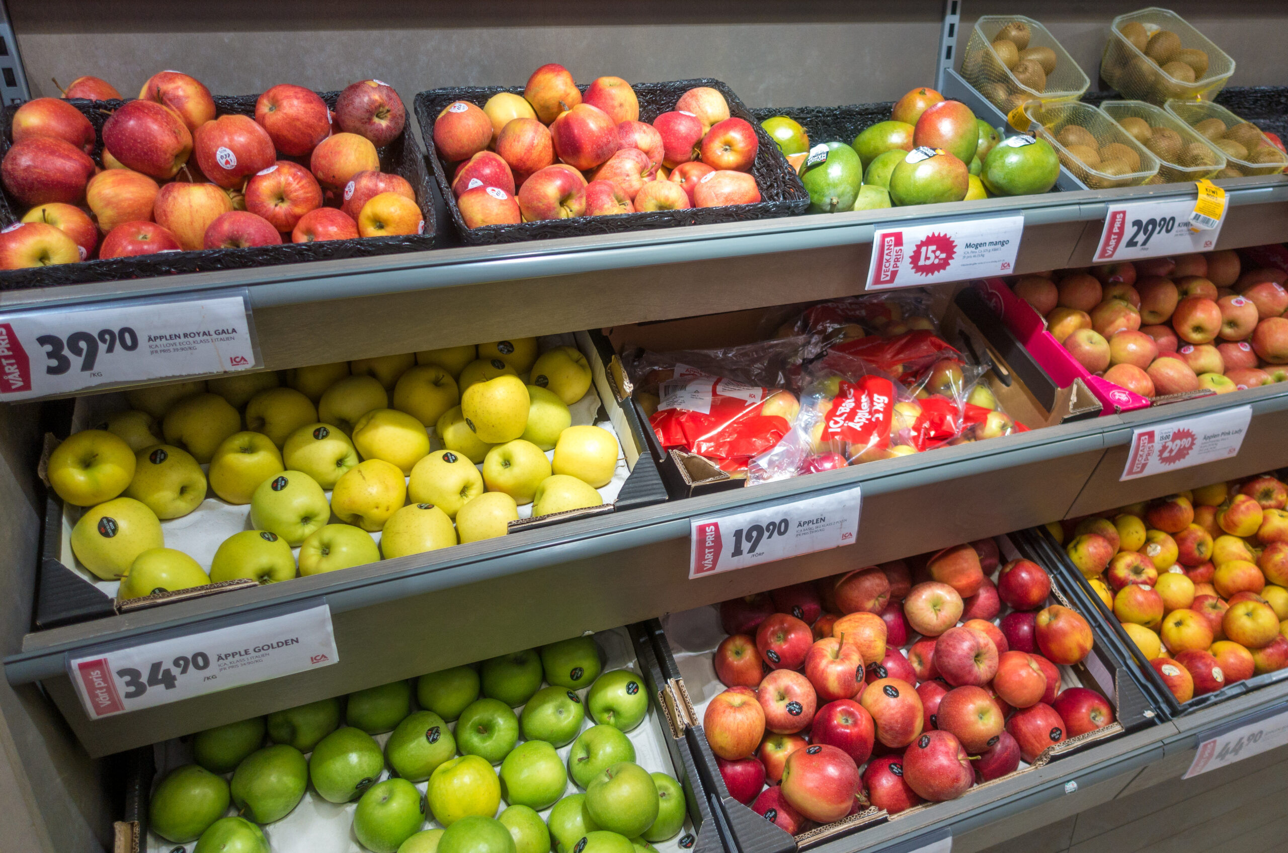 Bright grocery produce display with apples, pears, mangoes, and other fruit on supermarket shelves.