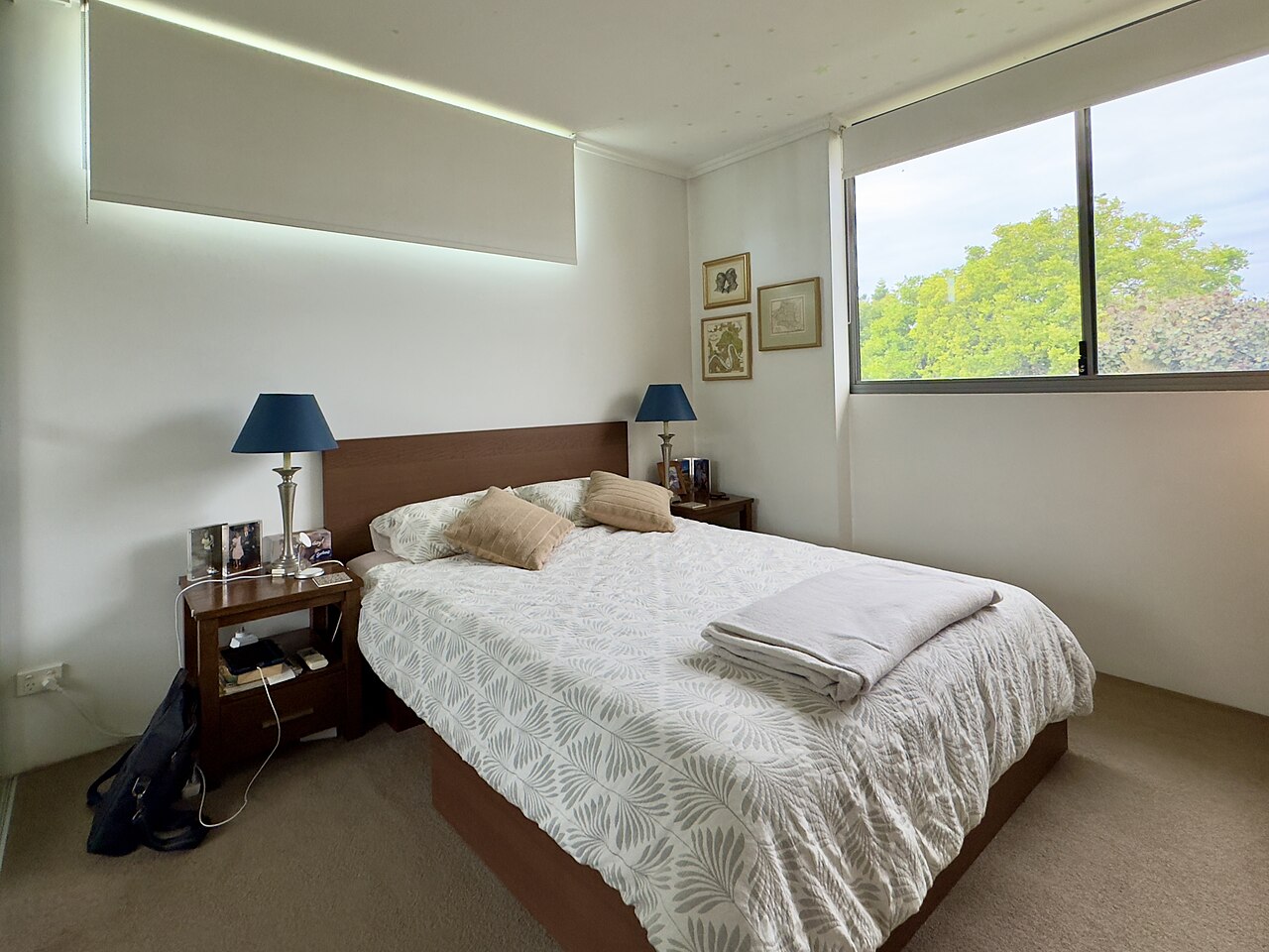 Simple apartment bedroom with a made bed, side table, and daylight from a window.