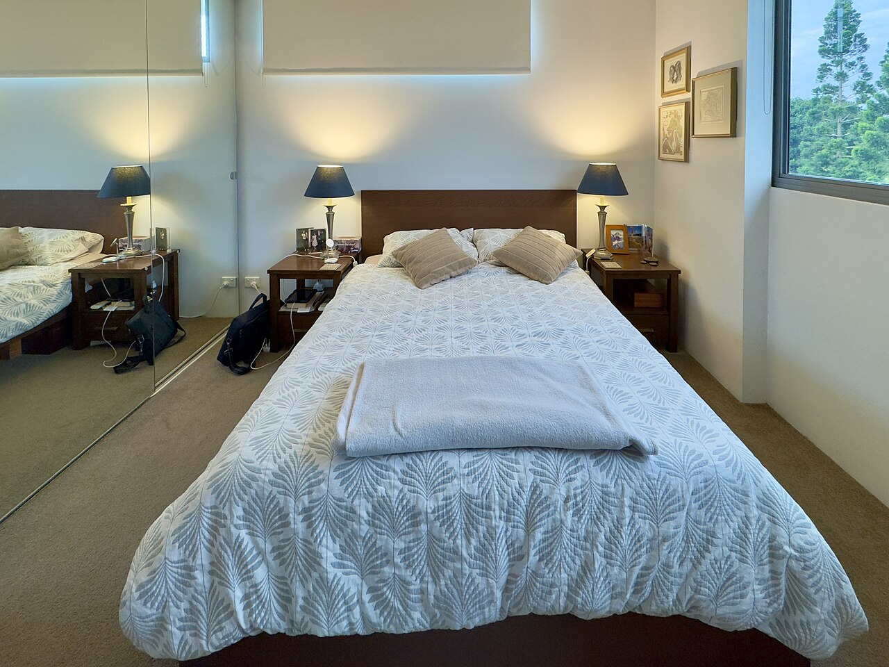 Simple apartment bedroom with bed, side table, and daylight from a window.