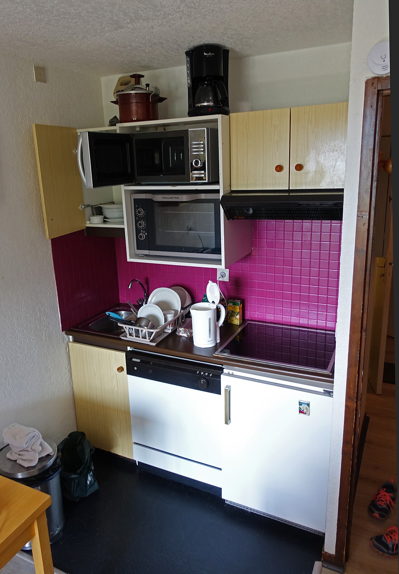 Compact apartment kitchenette with cabinets, sink, stove, and small table.