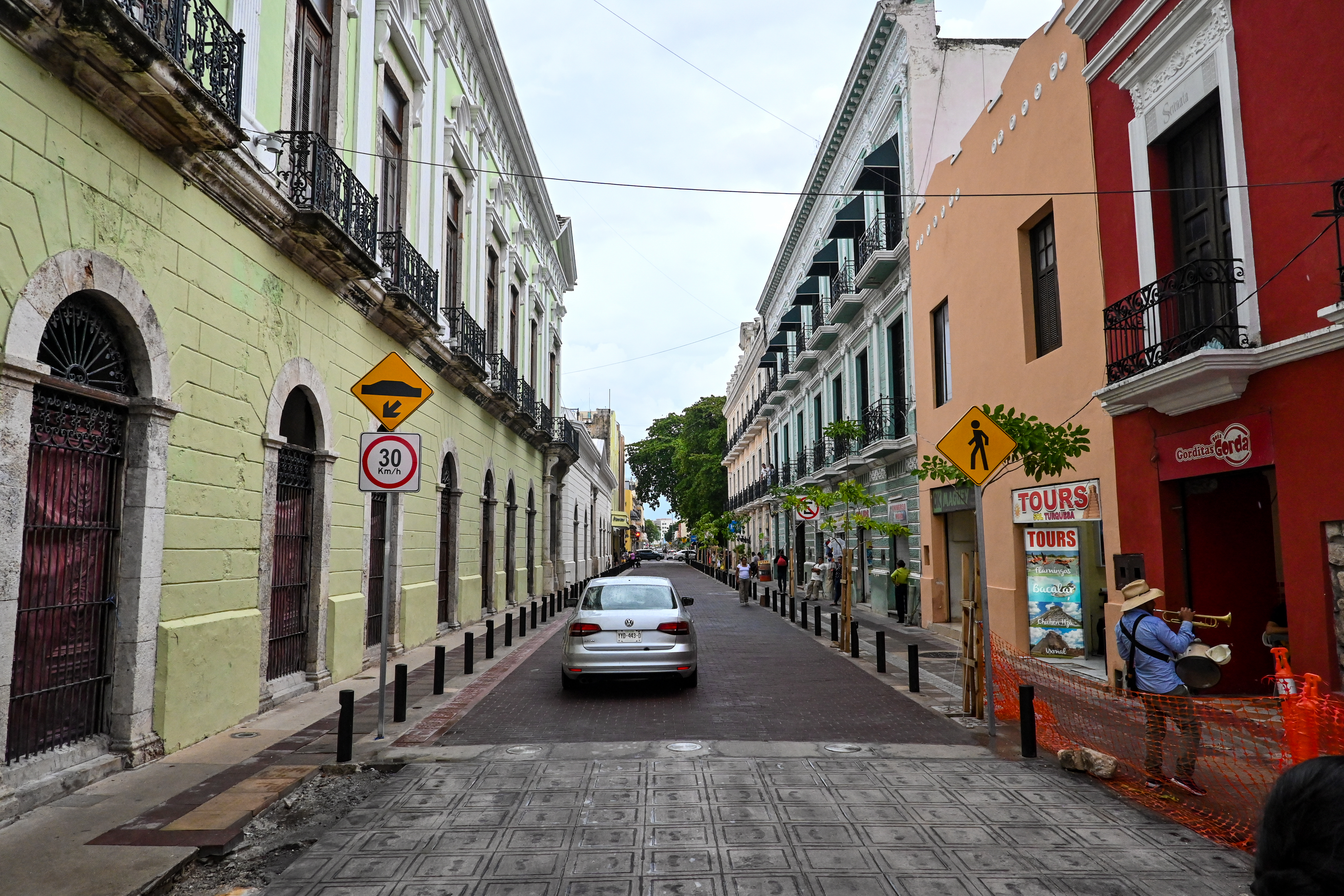Street scene in central Mérida with everyday traffic, storefronts, and low-rise buildings.