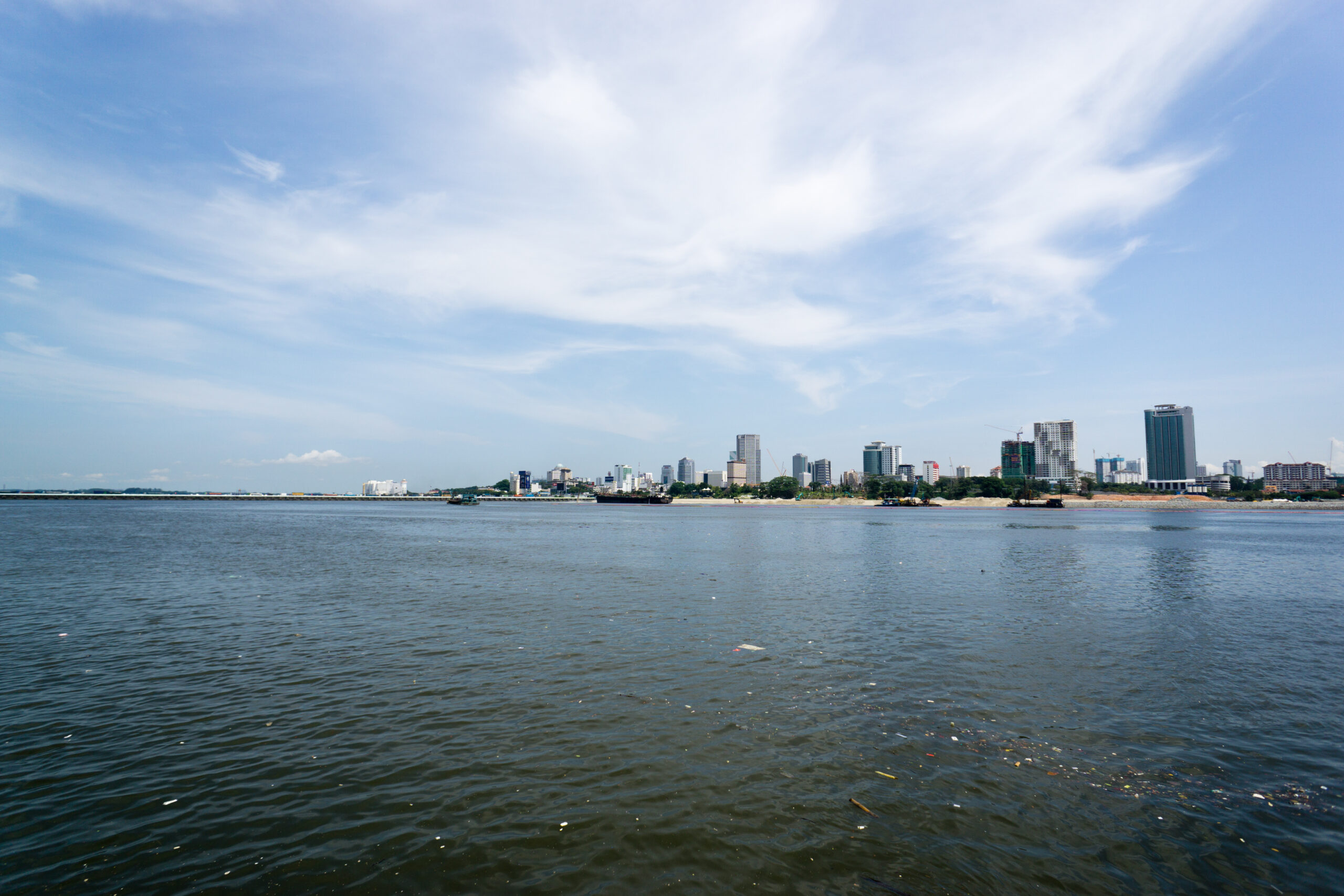Johor Bahru skyline with waterfront high-rises and a dense urban edge along the water.