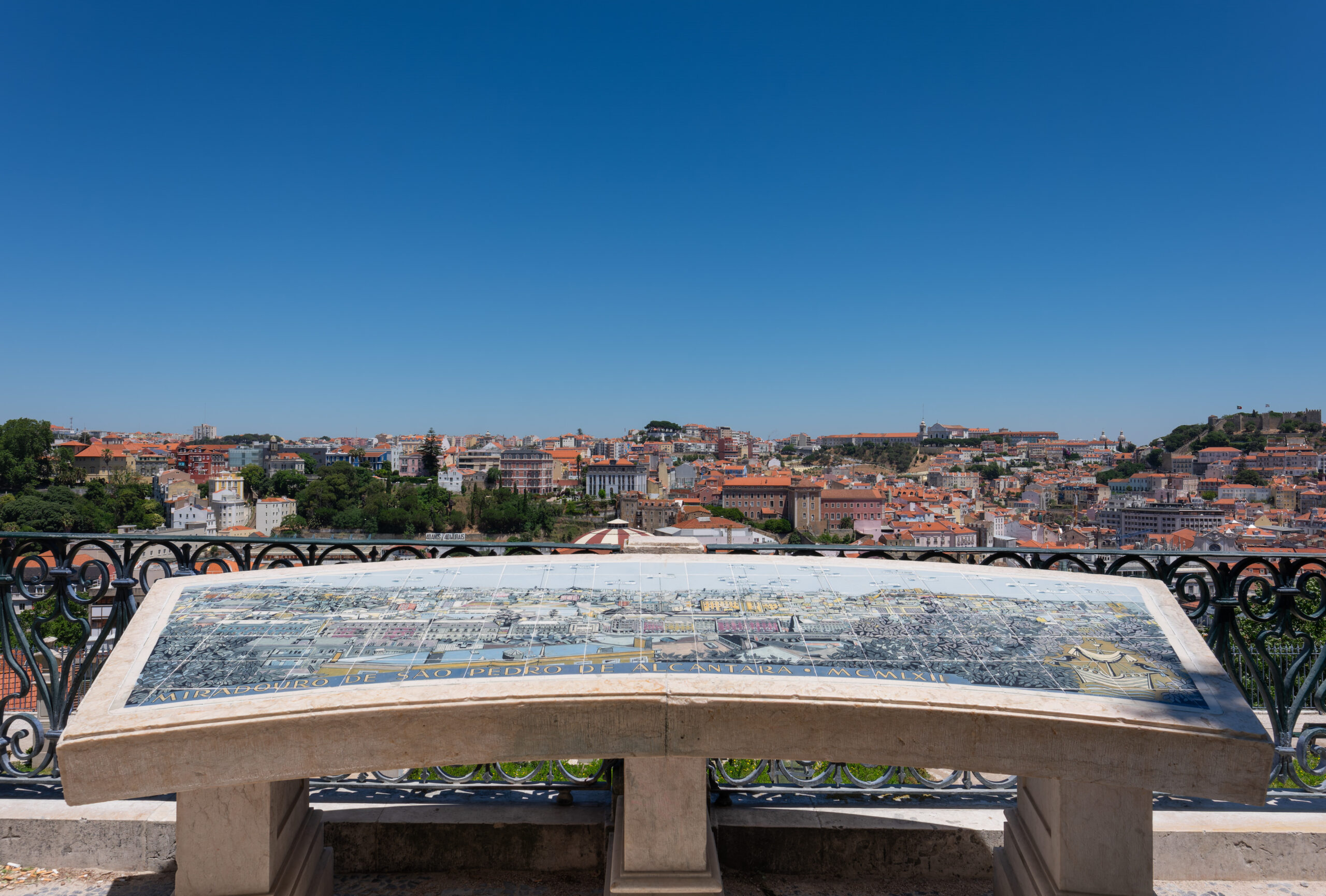 Panoramic viewpoint over Lisbon with tiled foreground and dense city rooftops beyond.