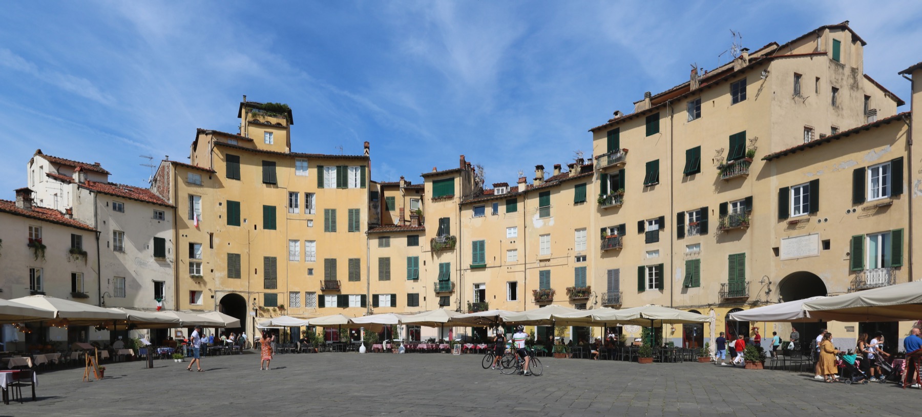 View into Piazza Anfiteatro in Lucca with pastel buildings and outdoor seating.