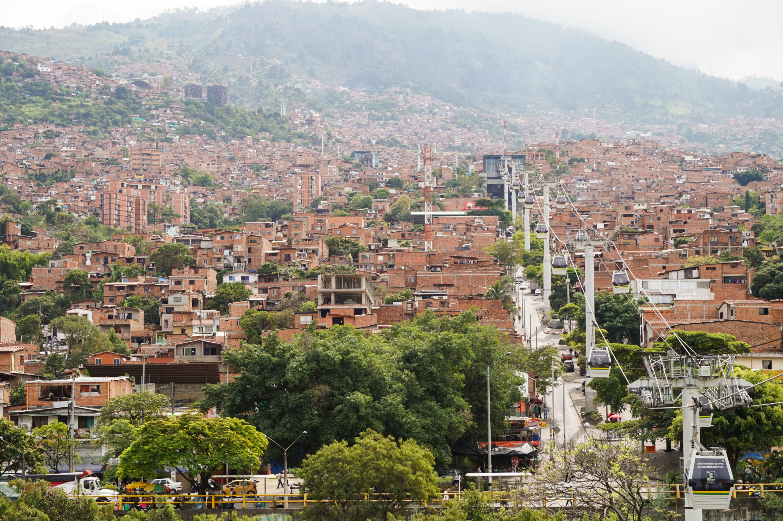 Line K Metrocable cabins moving above Medellín neighborhoods in daylight.