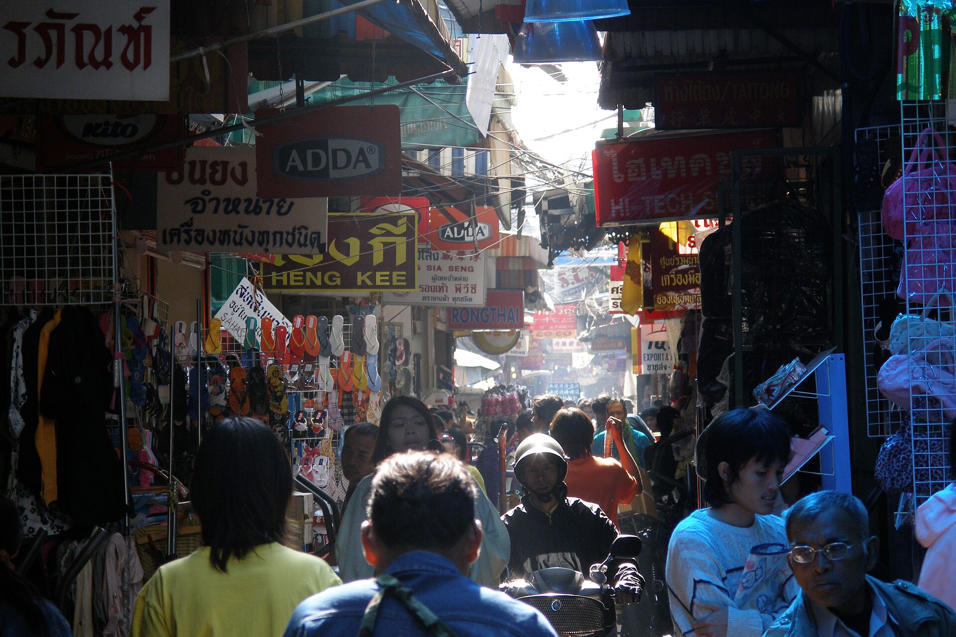 Busy lane in Bangkok Chinatown with pedestrians, market goods, and dense urban storefronts.