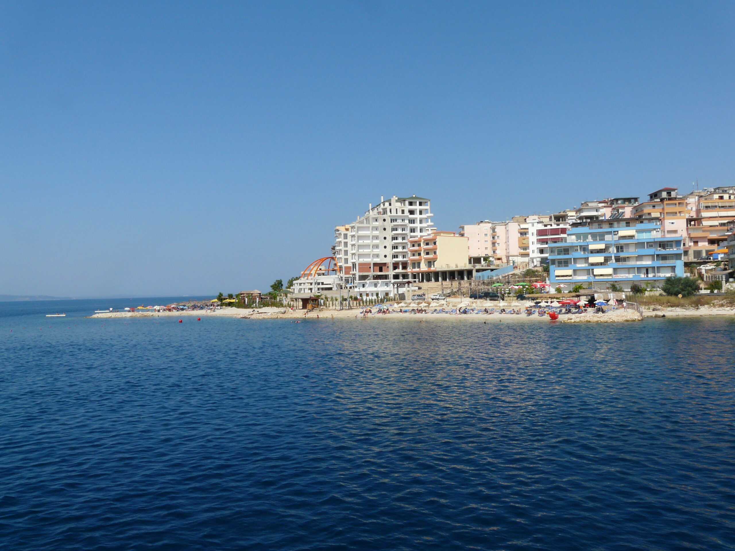Sunny waterfront view across the northern end of Saranda with bayfront buildings and beach below.