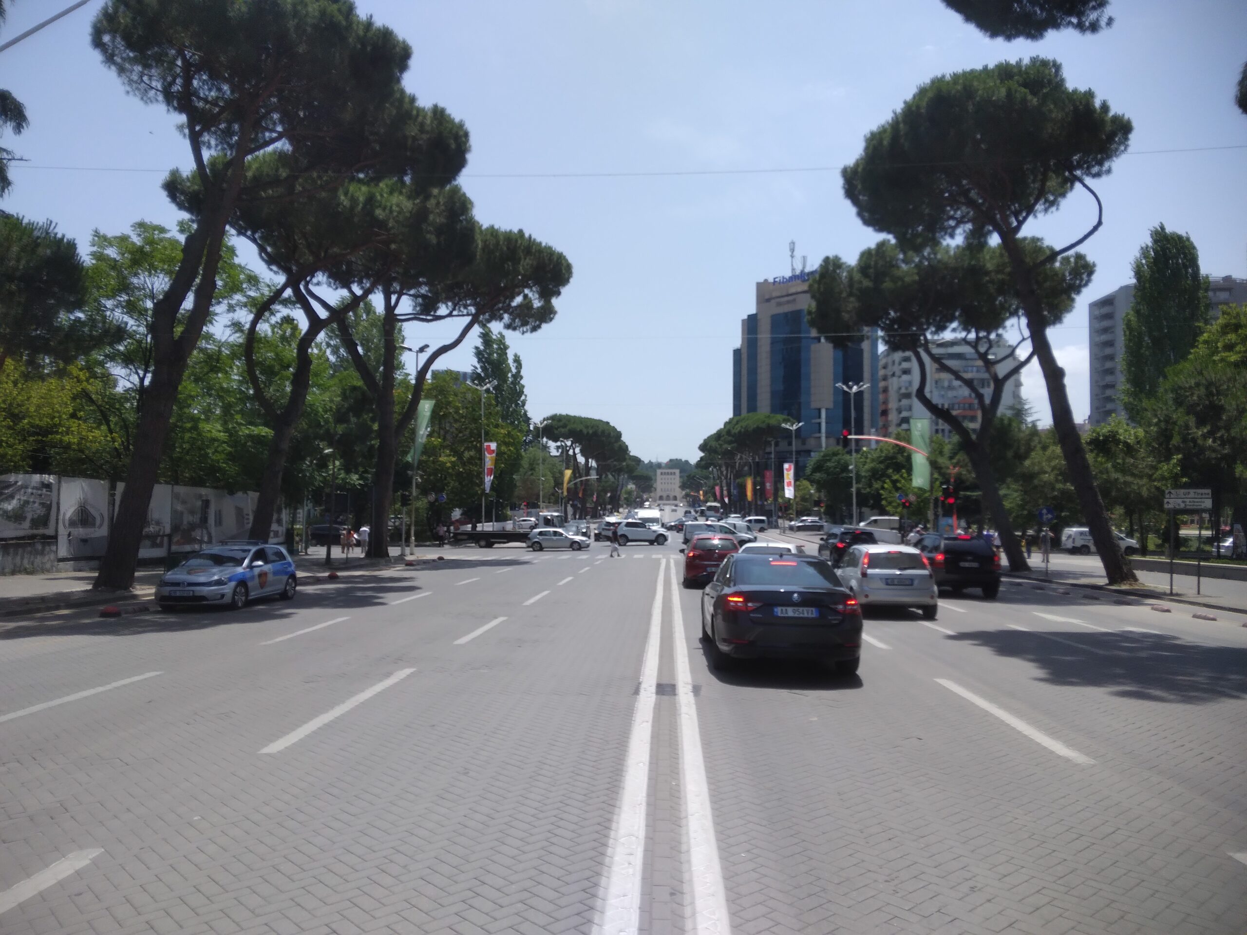 Broad central boulevard in Tirana lined with trees, civic buildings, and pedestrians.