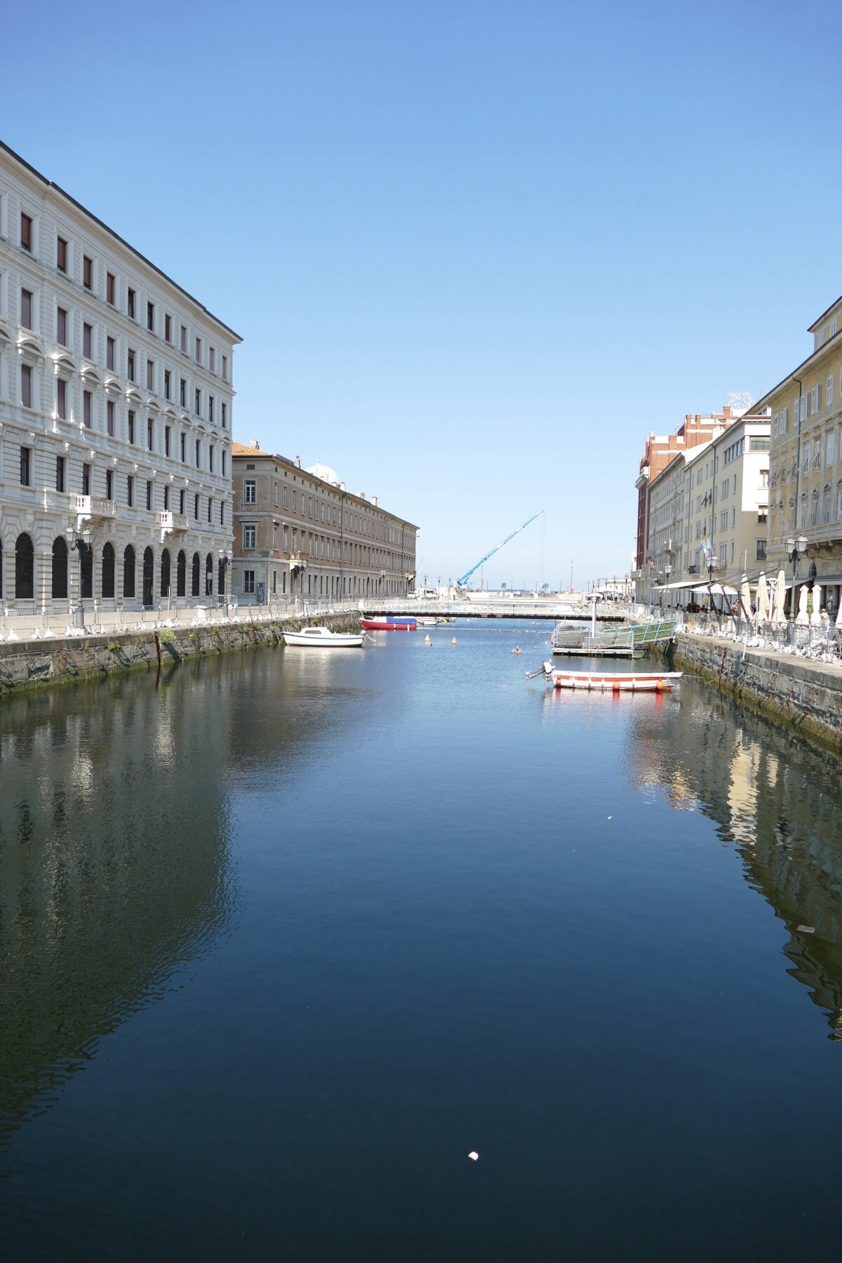 Sunny view along Canal Grande in Trieste with boats and historic buildings.