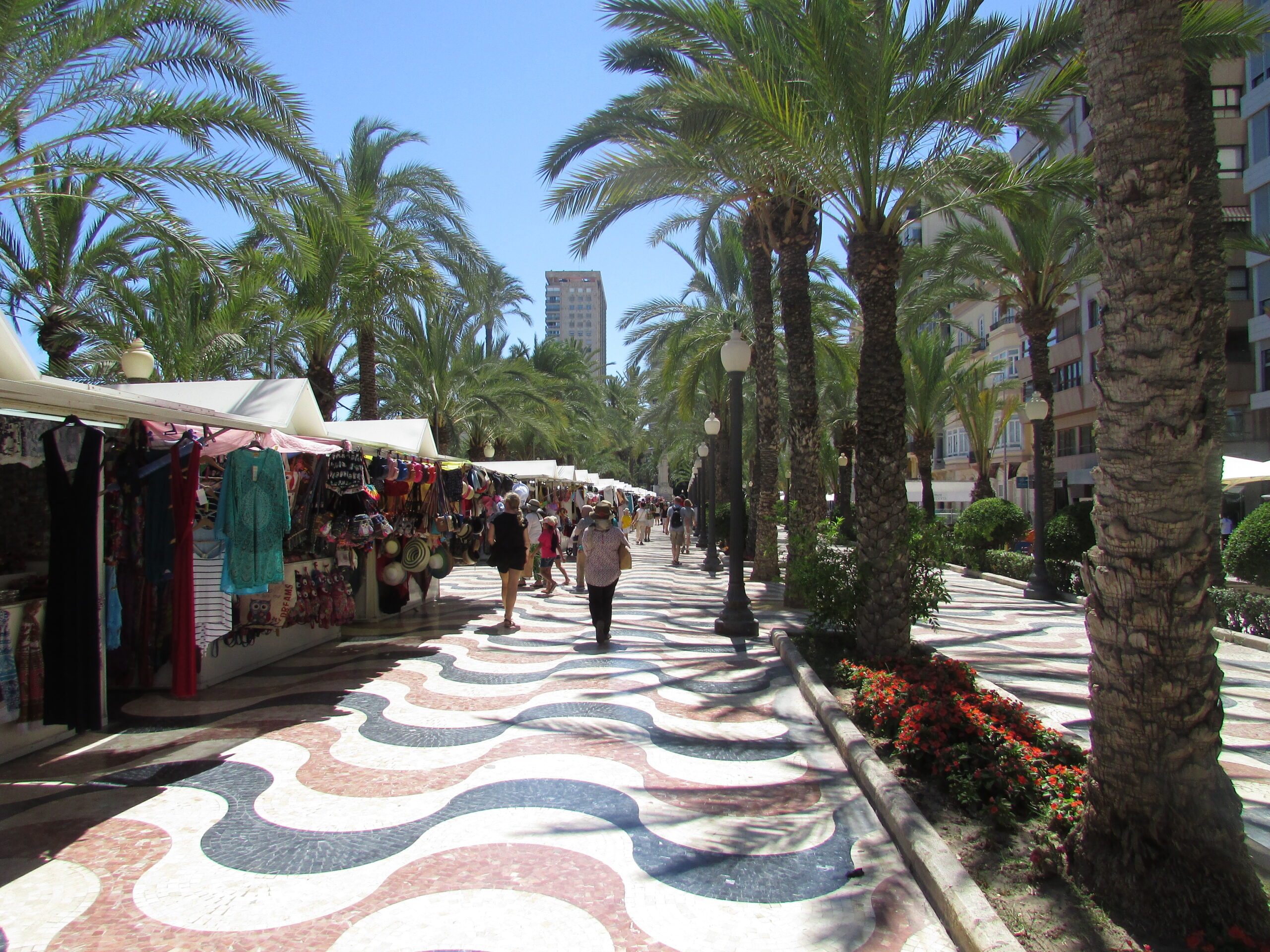 Market stalls and pedestrians on the Esplanada in Alicante, Spain, illustrating everyday walkable life beyond headline rent comparisons.