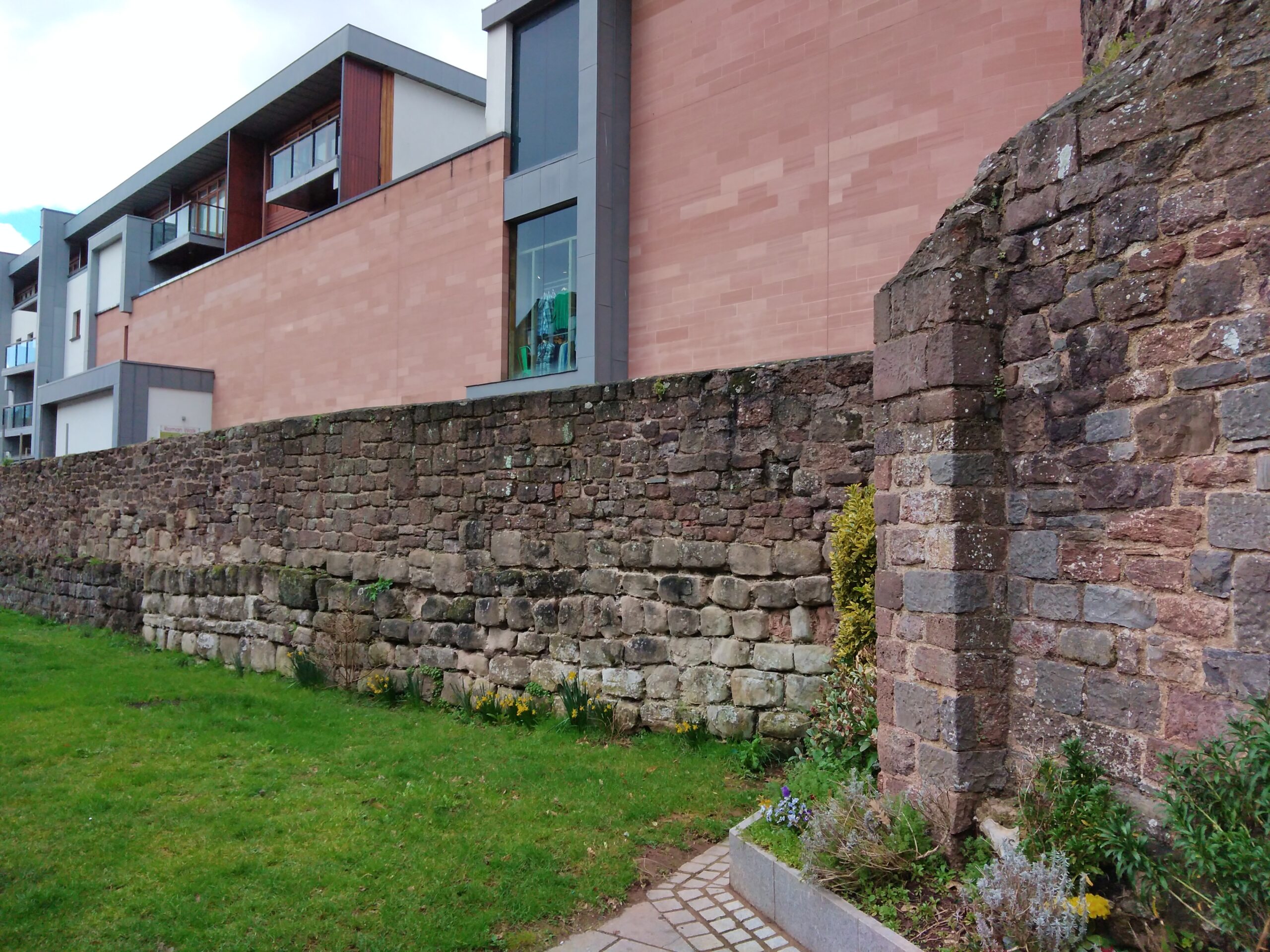 Shops and apartments behind a city wall in Exeter, illustrating why a shortlist should test whether housing, errands, and daily access overlap in a real neighborhood.