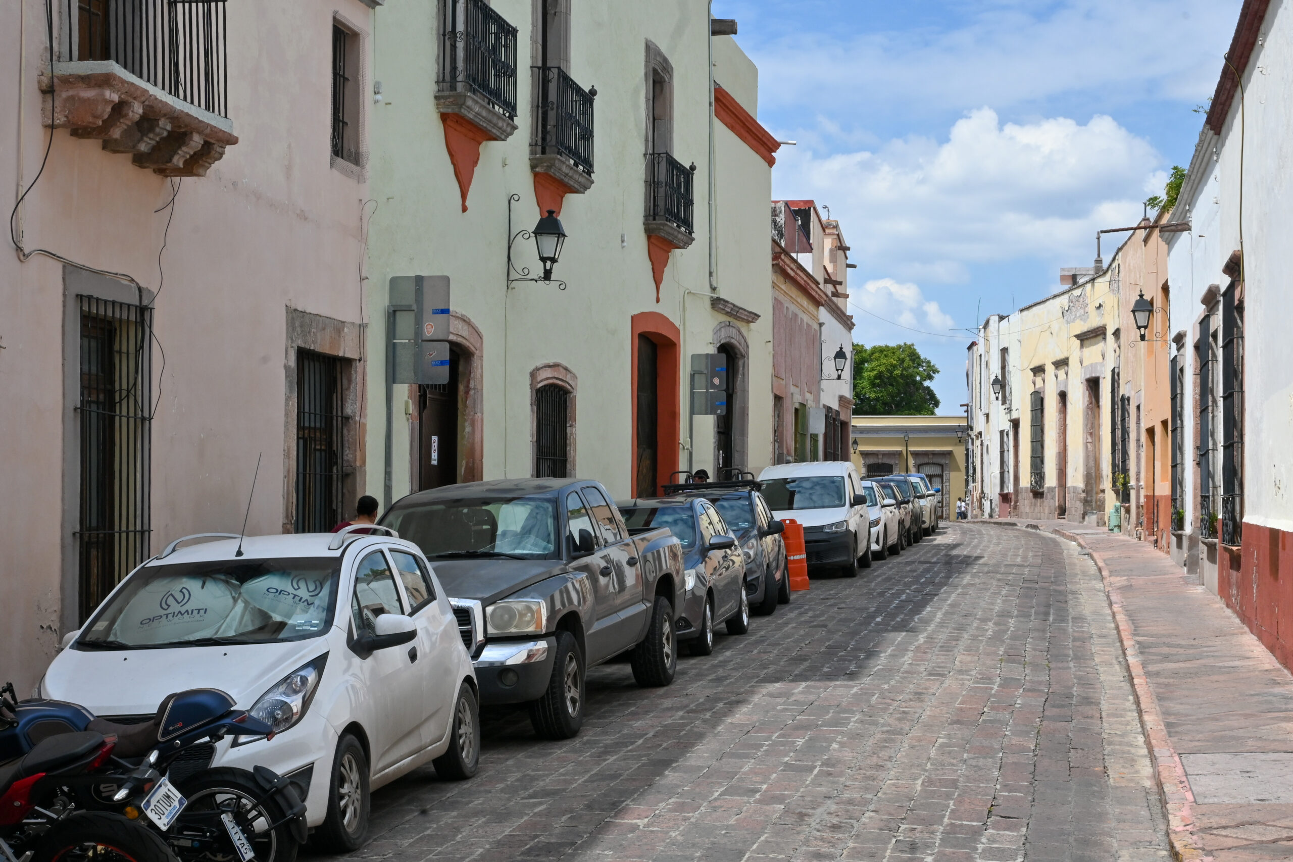 A central Querétaro street with parked cars, sidewalks, and older buildings, showing ordinary daily-life logistics.