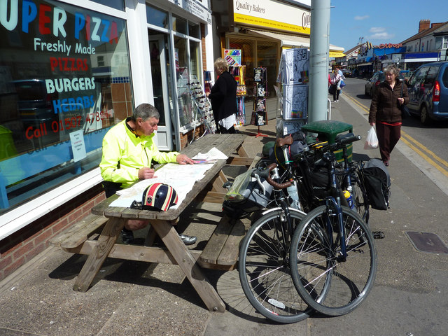 A cyclist reviewing paper route maps outside small shops while planning the next direction.