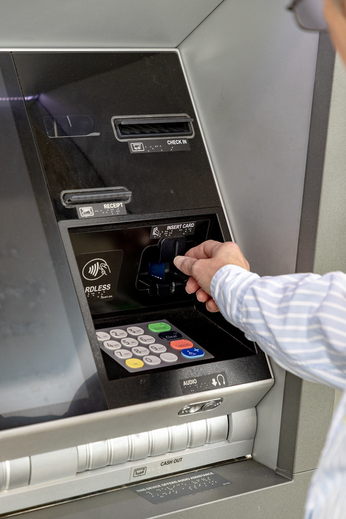 Person using a payment card at an ATM while managing backup access to cash abroad.