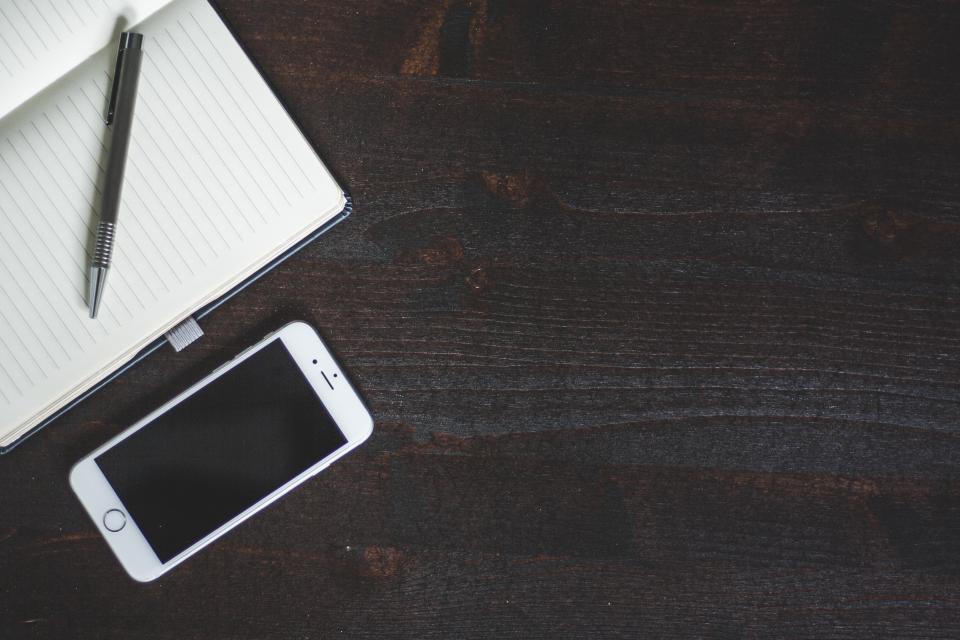 Notebook, pen, and phone arranged on a desk for travel backup planning.