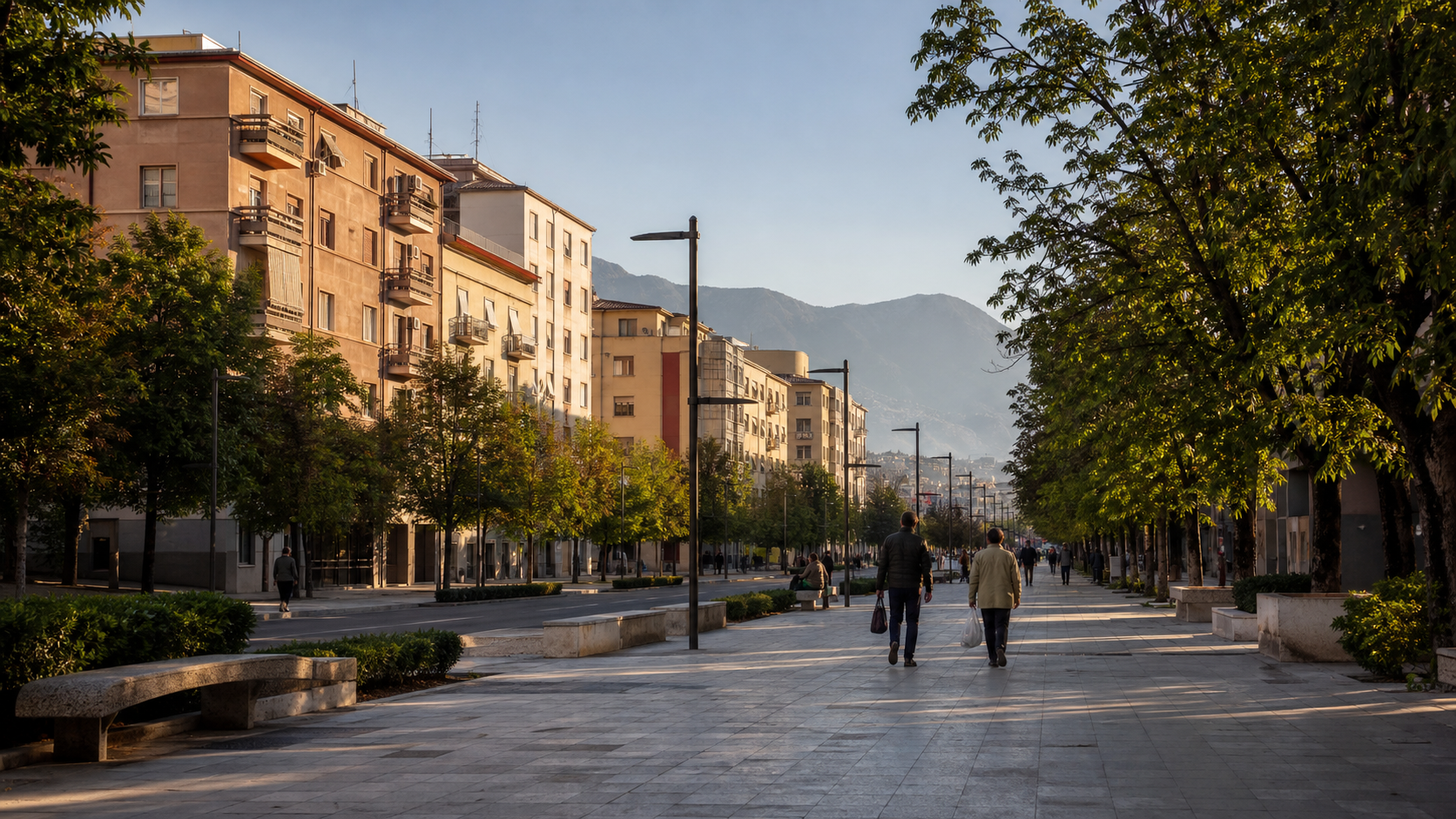 Tree-lined Tirana boulevard with apartment buildings, pedestrians, and distant mountains in morning light.
