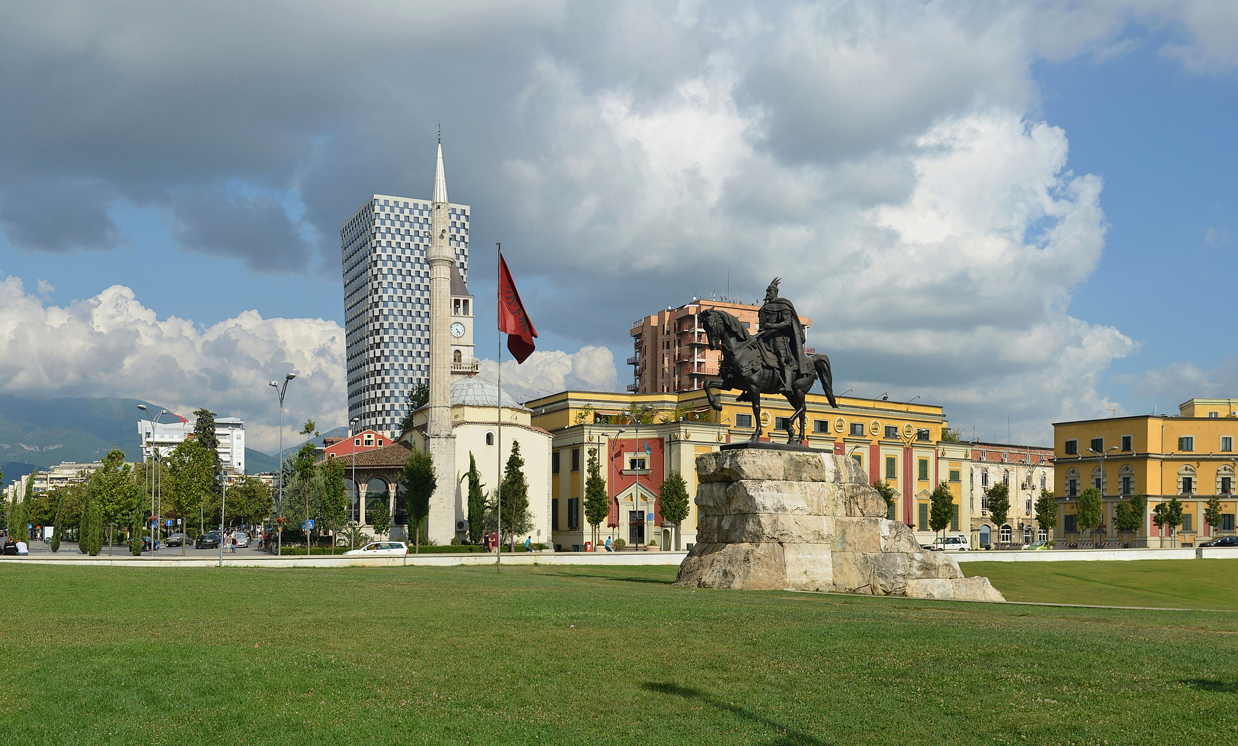 Skanderbeg Square in central Tirana with the Albanian flag, mosque, clock tower, and city landmarks in view.