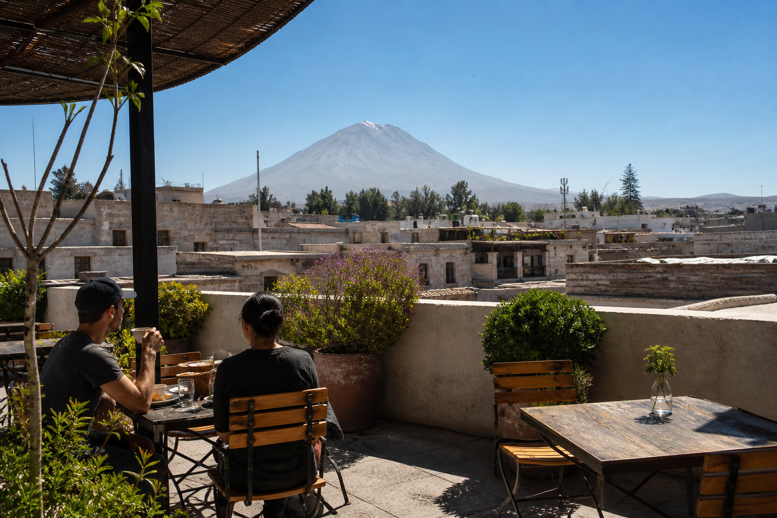 Two adults enjoy coffee on a shaded Arequipa rooftop terrace with white stone rooftops and Misti volcano beyond.