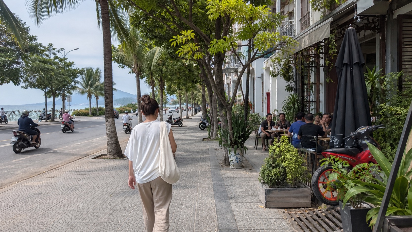 A pedestrian walks along a palm-lined Da Nang neighborhood street near cafés and the coast.