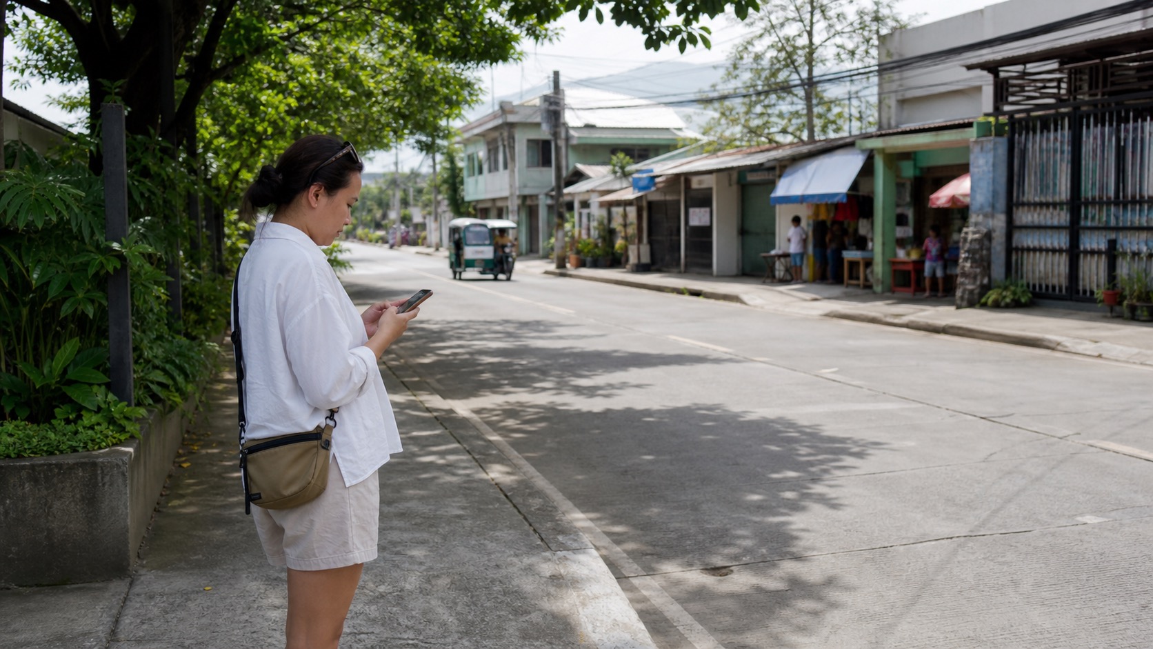Traveler checking a phone route beside a shaded ordinary street in Iloilo, Philippines.